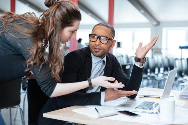 dois jovens, um homem, e uma mulher em uma mesa de escritório discutindo a escolha adequada de um wms no notebook.