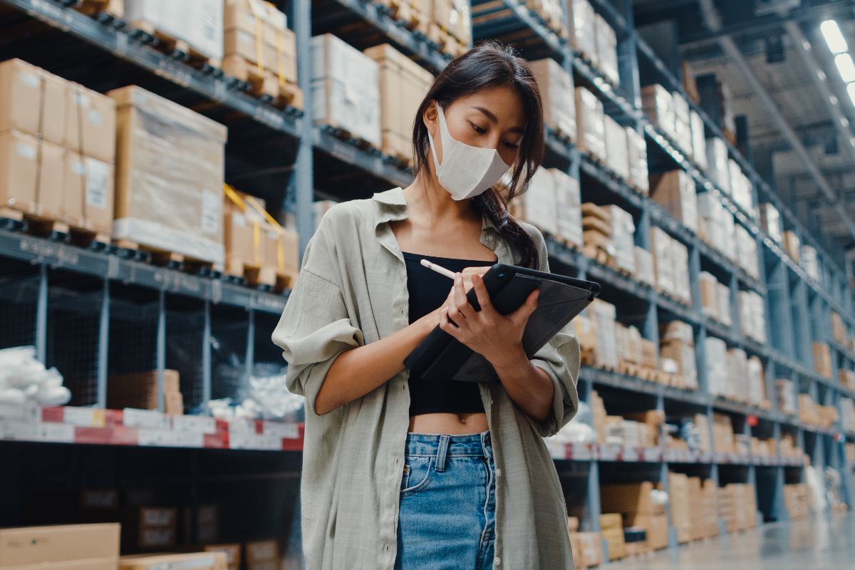 mulher de máscara em um depósito checando lista