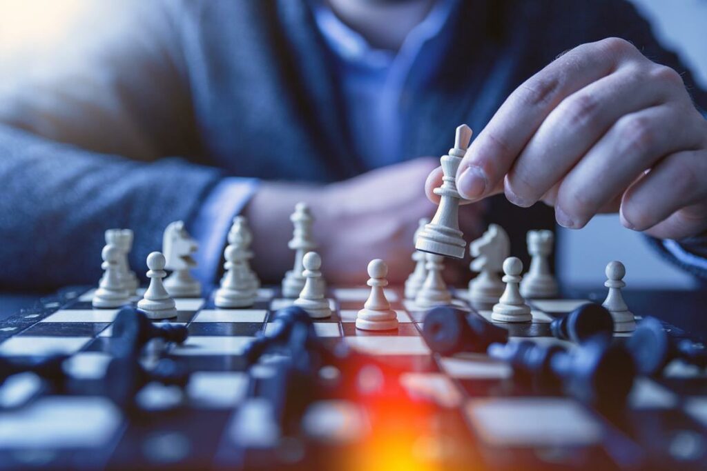 imagem de uma mesa com um jogo de xadrez e um homem ao fundo jogando, imagem desfocada.